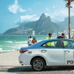 Viatura policial circula pela orla de Ipanema, no Rio de Janeiro, com os Dois Irmãos ao fundo.