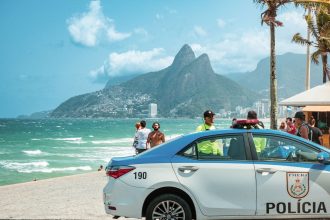 Viatura policial circula pela orla de Ipanema, no Rio de Janeiro, com os Dois Irmãos ao fundo.