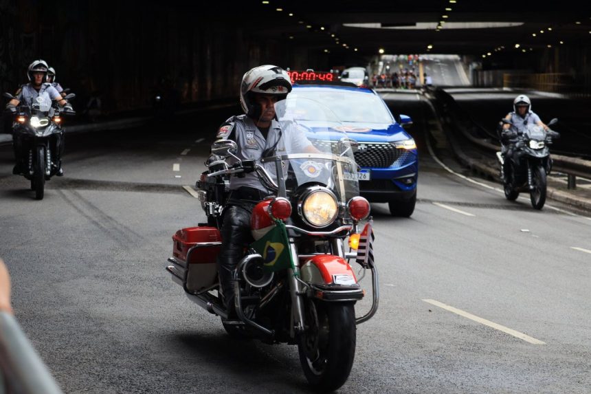Equipe de motociclistas policiais escolta veículos durante a passagem por um túnel urbano.