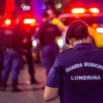 Agente da guarda municipal em serviço durante a noite, em uma rua iluminada.