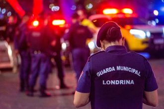 Agente da guarda municipal em serviço durante a noite, em uma rua iluminada.