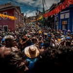 Multidão participa de uma animada festa de rua de Carnaval no Rio de Janeiro, cercada por decoração colorida.