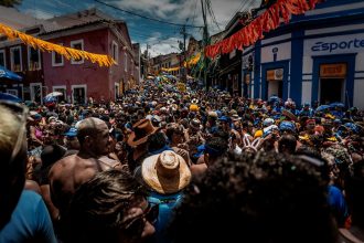 Multidão participa de uma animada festa de rua de Carnaval no Rio de Janeiro, cercada por decoração colorida.