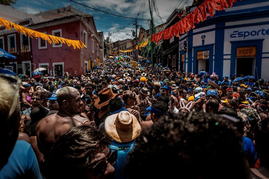 Multidão participa de uma animada festa de rua de Carnaval no Rio de Janeiro, cercada por decoração colorida.
