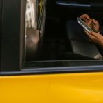Passageiro usa o celular no banco traseiro de um táxi enquanto o motorista dirige.