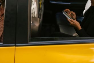 Passageiro usa o celular no banco traseiro de um táxi enquanto o motorista dirige.