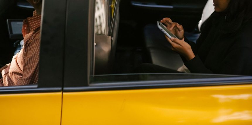 Passageiro usa o celular no banco traseiro de um táxi enquanto o motorista dirige.