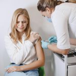 Profissional de saúde aplica uma vacina no braço de uma paciente em uma clínica.