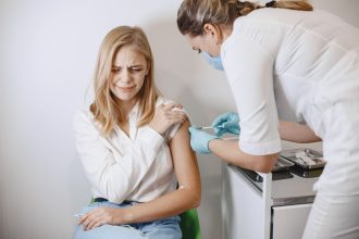 Profissional de saúde aplica uma vacina no braço de uma paciente em uma clínica.