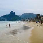 Turistas aproveitam um dia ensolarado na praia de Ipanema, no Rio de Janeiro, com o Morro Dois Irmãos ao fundo.