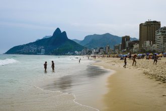 Turistas aproveitam um dia ensolarado na praia de Ipanema, no Rio de Janeiro, com o Morro Dois Irmãos ao fundo.